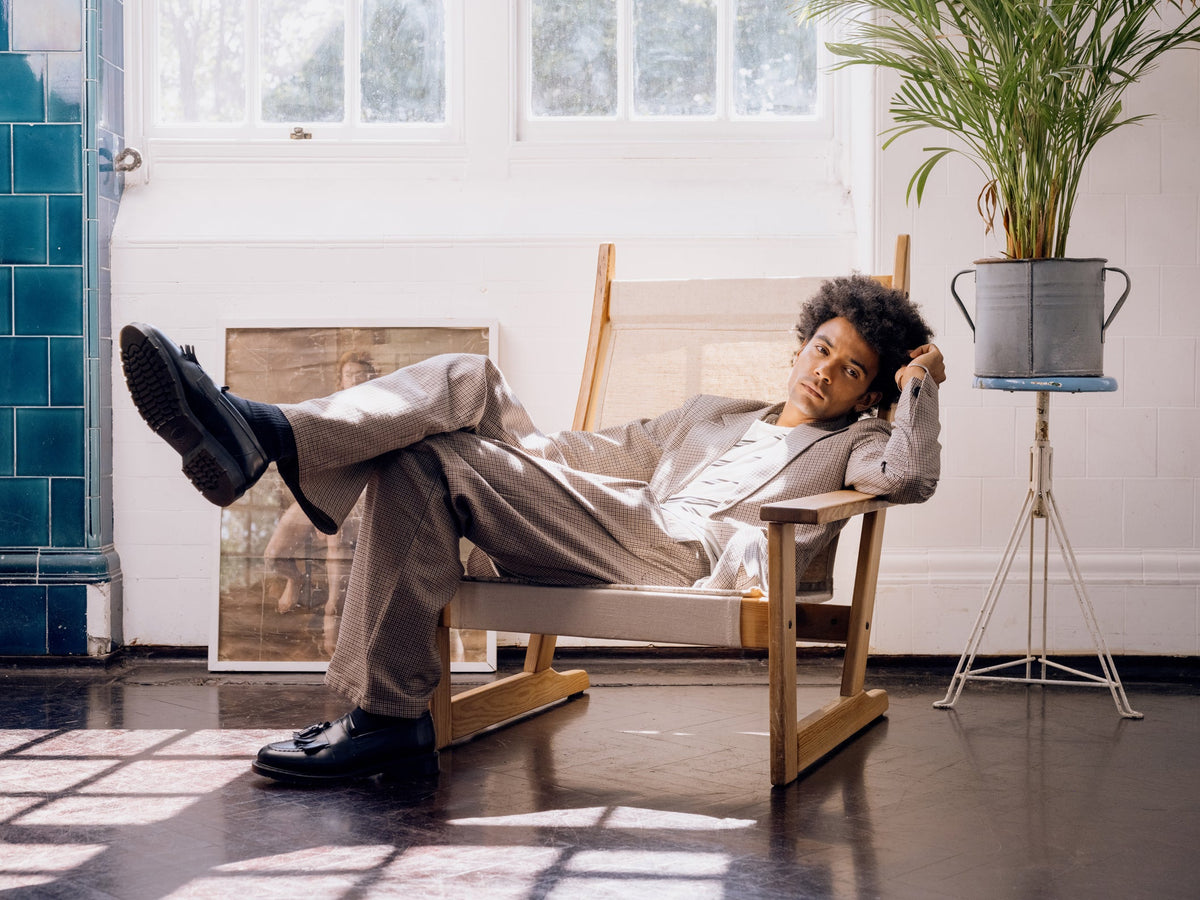 Model wearing a light beige unstructured linen blazer with matching tailored trousers, shirt and tie, showcasing relaxed modern tailoring by Oliver Spencer.