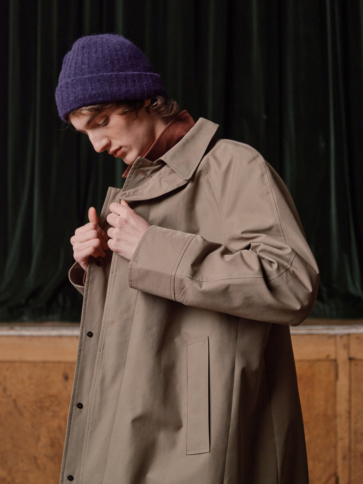 Man in a purple wool beanie fastening a stone cotton trench coat
