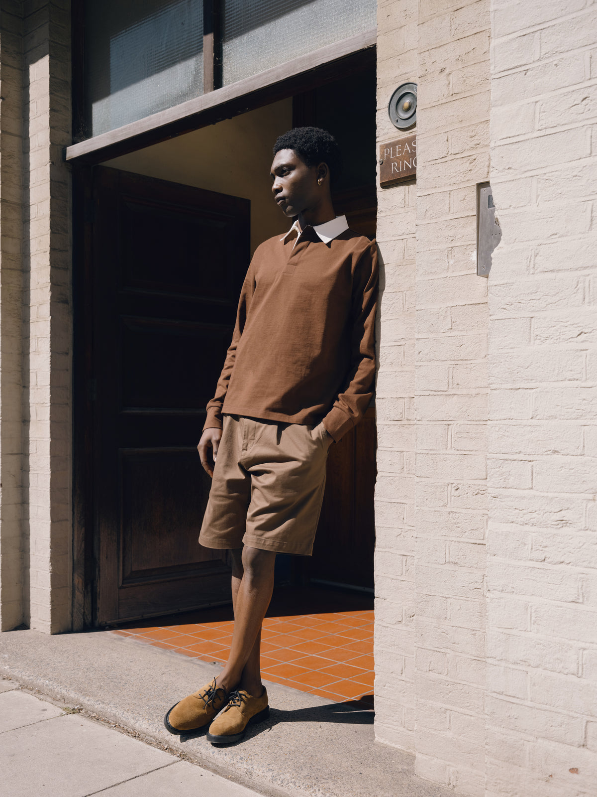 Brown long sleeve rugby top with brown shorts, standing in a dark doorway.