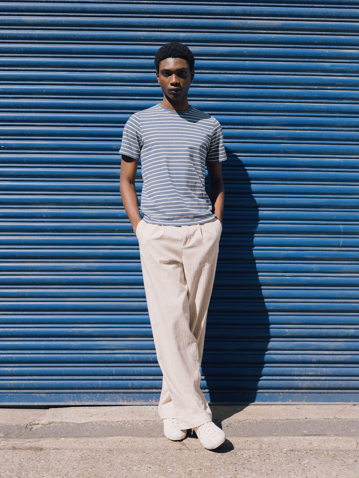 Blue and white striped Conduit T-shirt with cream trousers against a blue shutter.