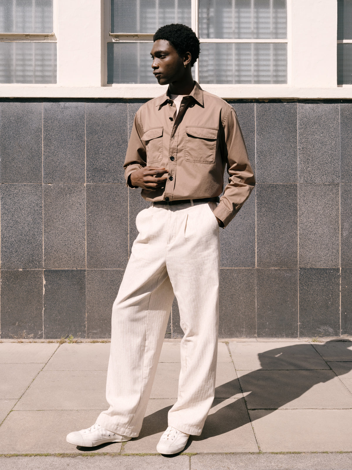Beige overshirt over a pink Conduit T-shirt with cream trousers, tiled wall behind.
