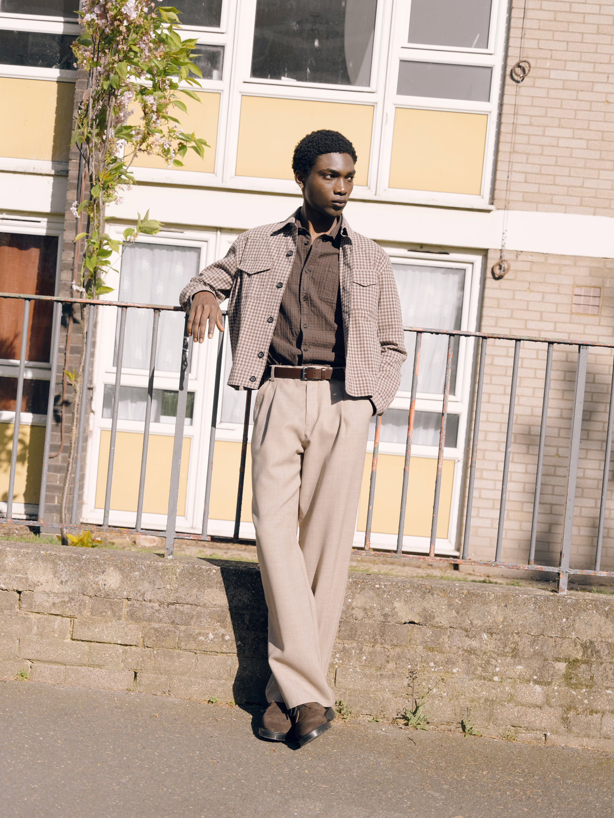 Brown Witley jacket over a brown shirt with beige Orsman trousers, railings and a yellow building behind.