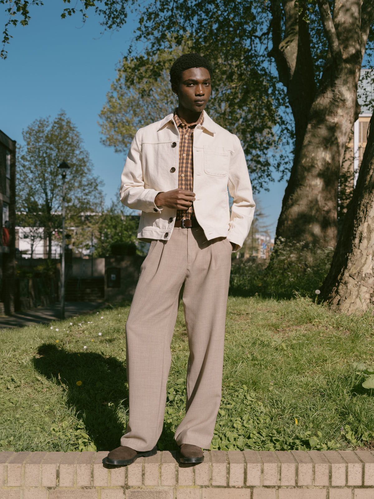 Ecru Buffalo jacket over a striped shirt with beige Orsman trousers, grass and a tree behind.
