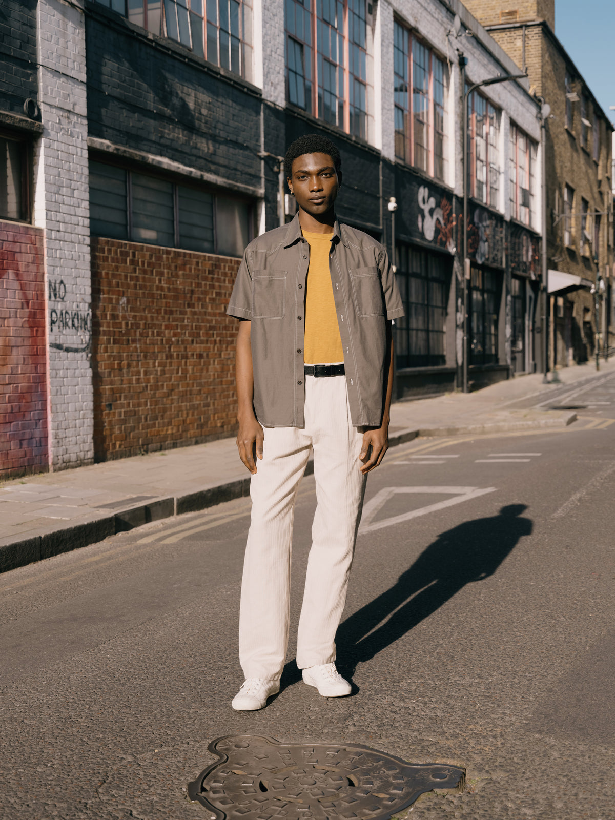 Green short sleeve shirt over an ochre T-shirt with cream Morton trousers, on the street.
