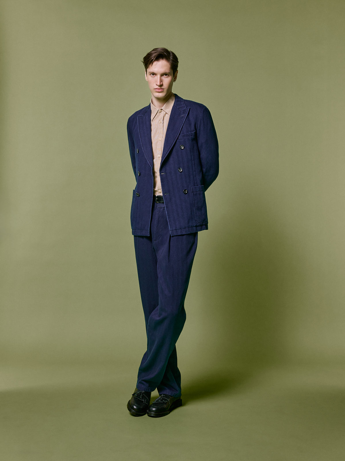 Navy double breasted suit with an open collar shirt, photographed against an olive backdrop.
