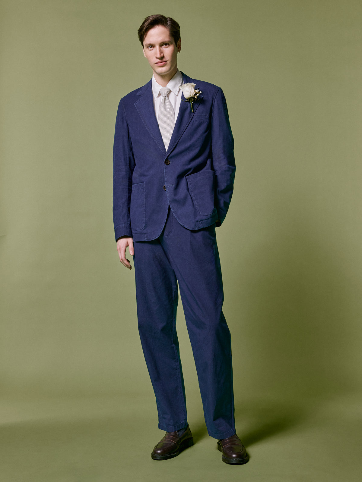 Indigo suit with a white shirt and tie, against an olive backdrop.