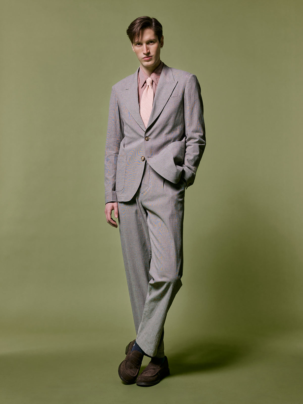 Brown and white check suit with a pink shirt and tie, against an olive backdrop.