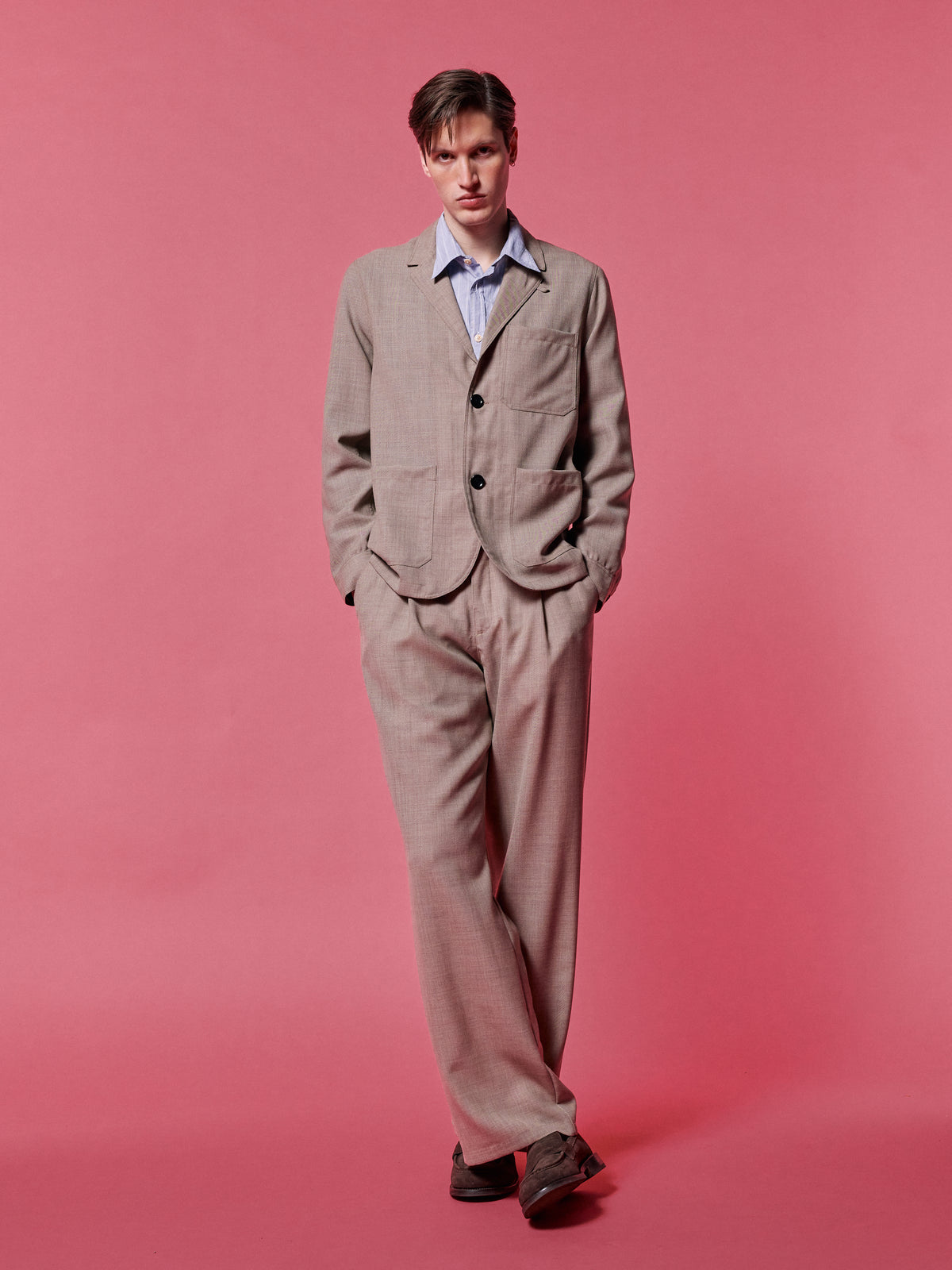 Stone suit over a blue shirt, against a pink backdrop.