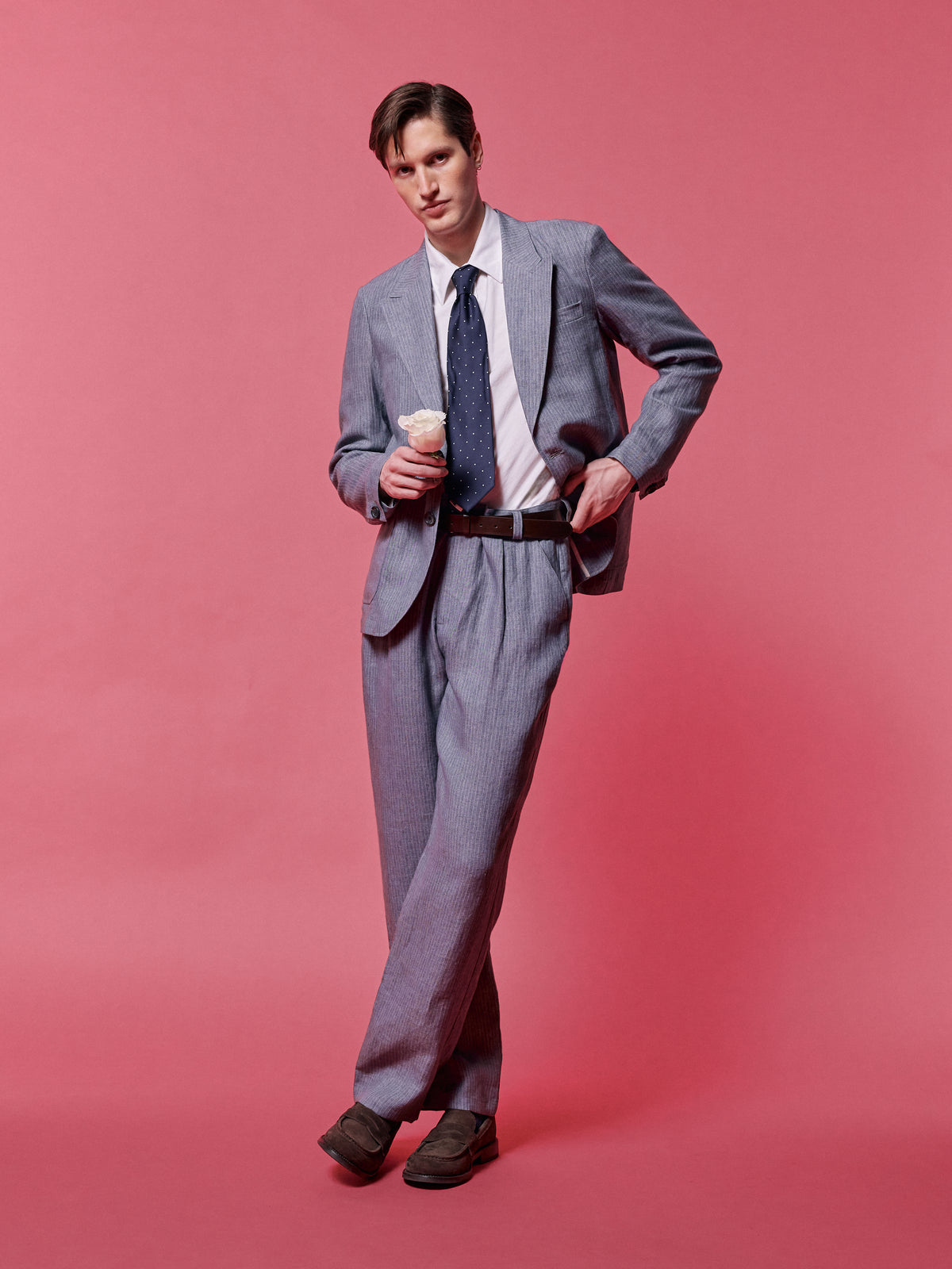 Grey suit with a white shirt and spotted tie, against a pink backdrop.
