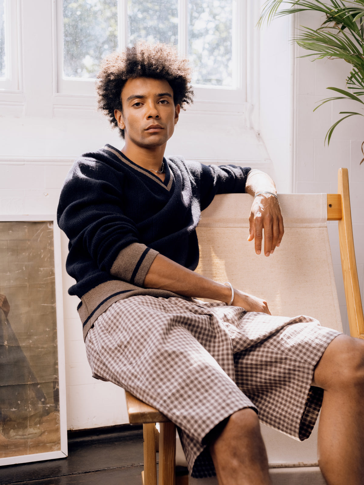 Navy V-neck jumper with contrast tipping and houndstooth legwear, seated.