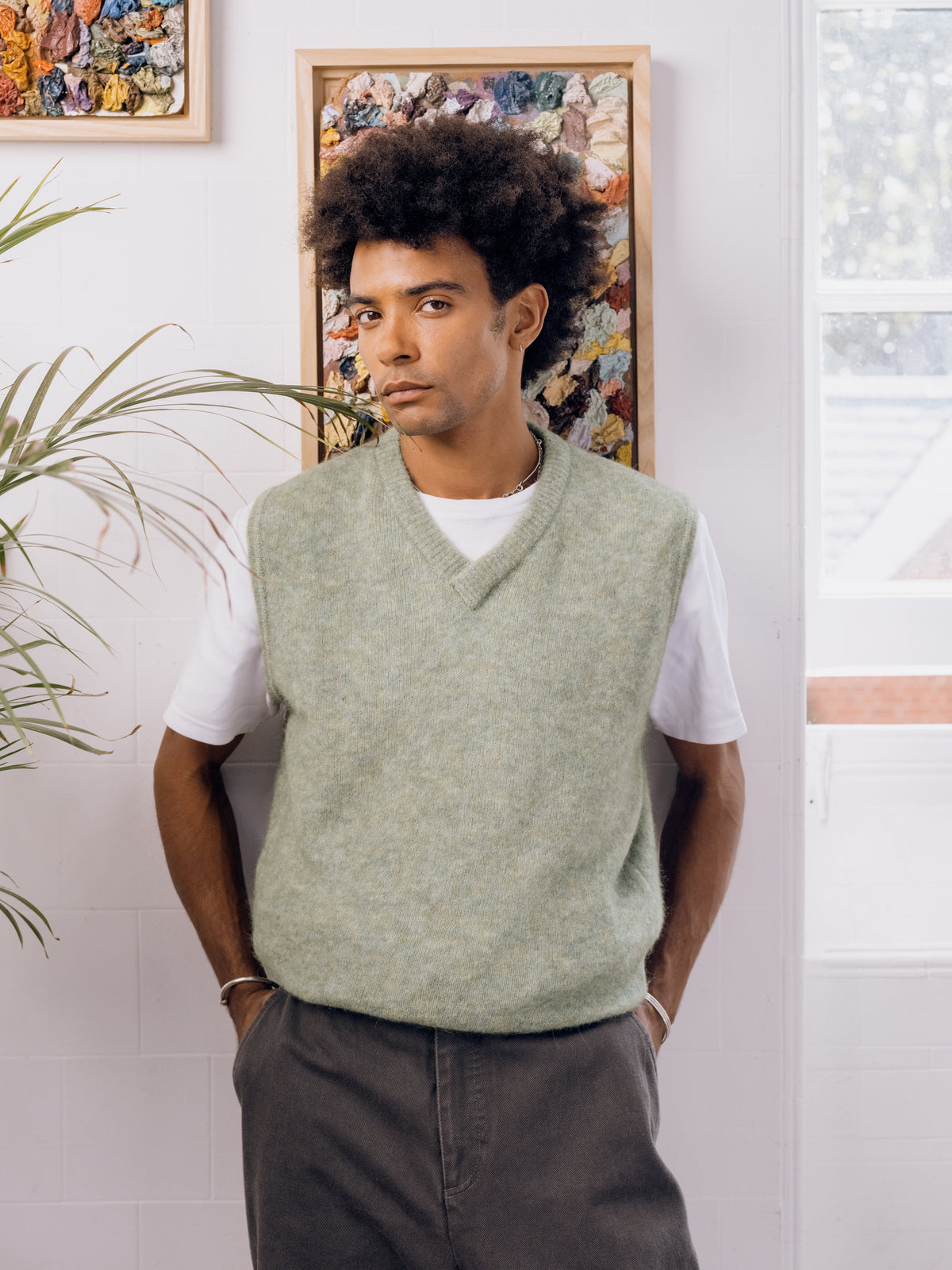 Sage knitted vest over a white T-shirt with grey Utility trousers.
