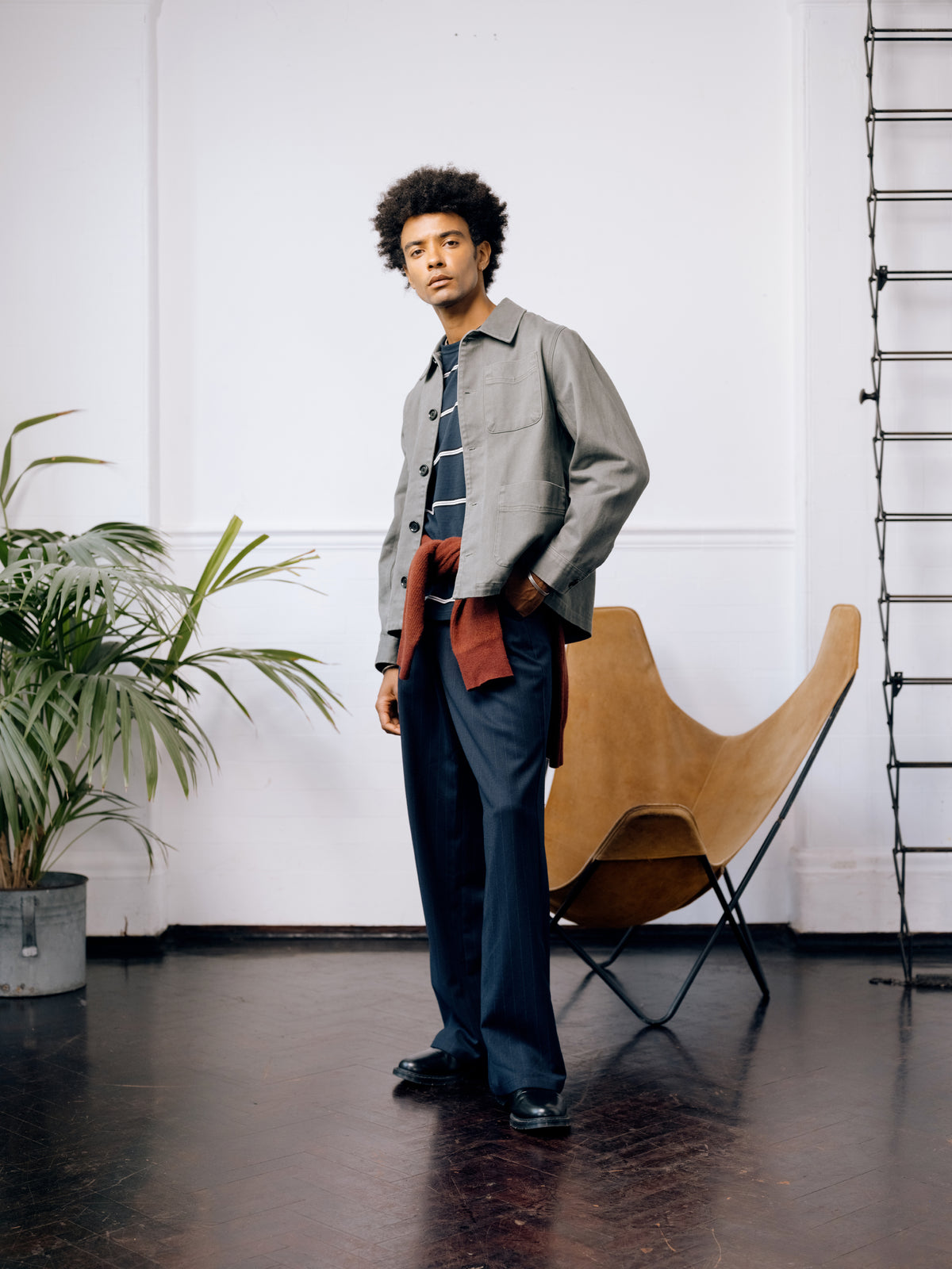 Green Kennard jacket over a navy striped T-shirt with a red jumper tied at the waist and navy pinstripe trousers.