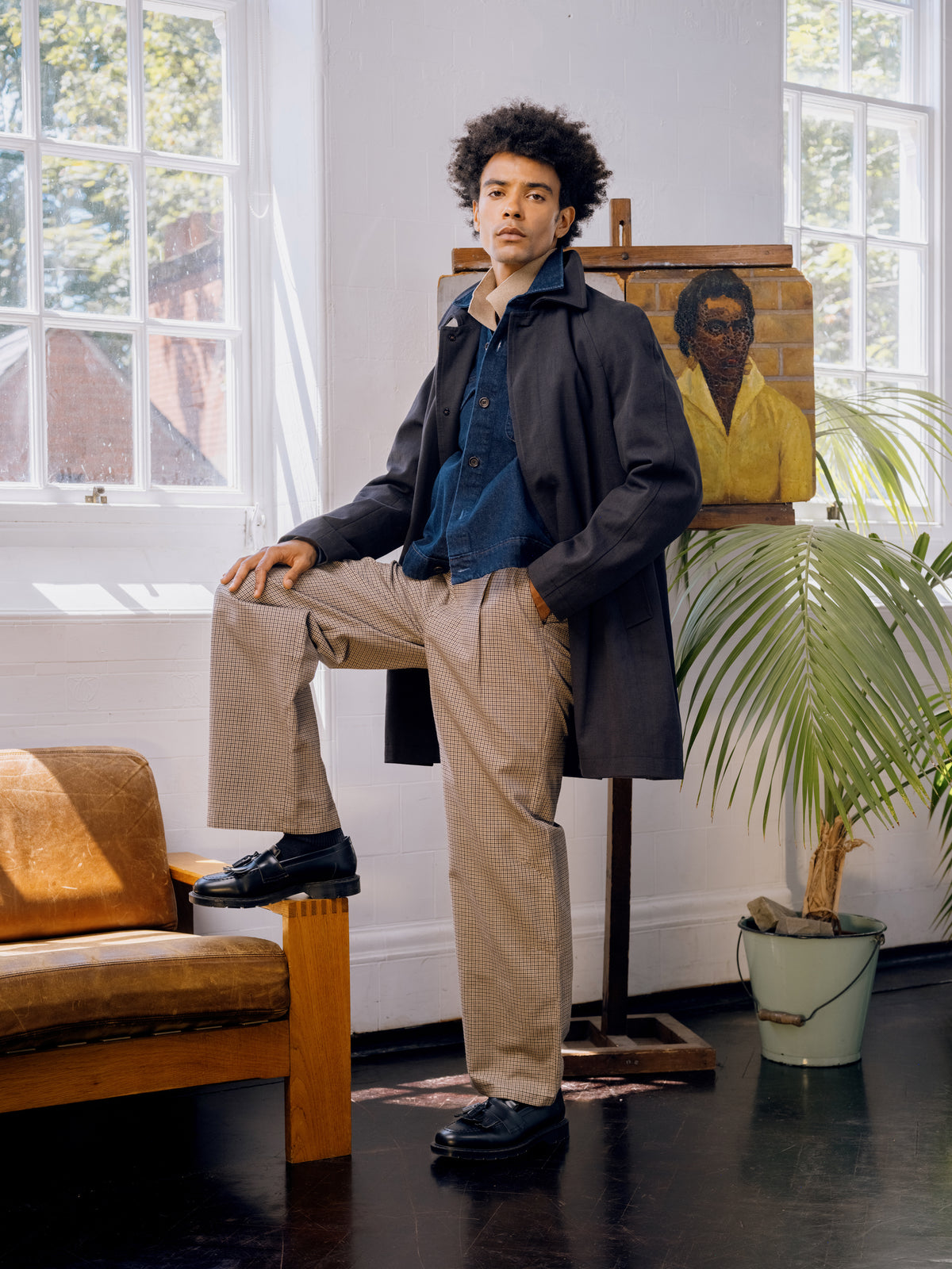 Graphite Lothian coat over a denim shirt with houndstooth trousers, one foot raised on a chair.