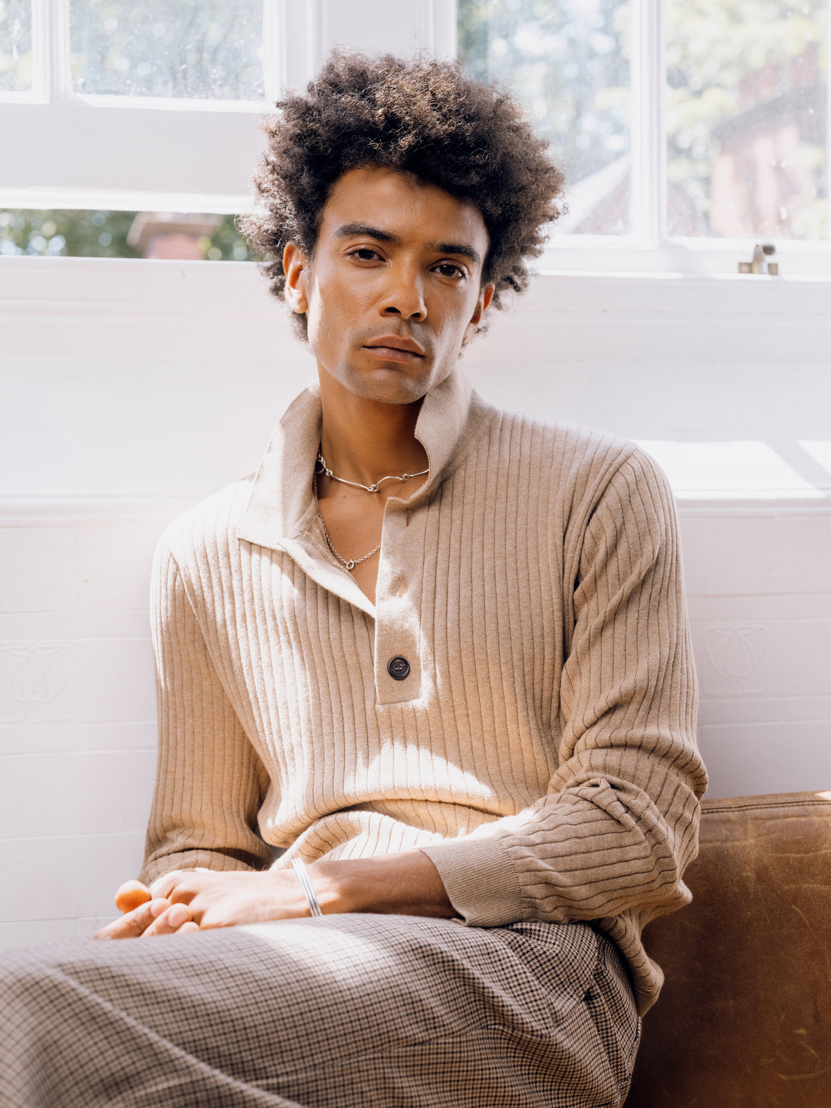 Sand Pablo knitted polo shirt with houndstooth trousers, seated.