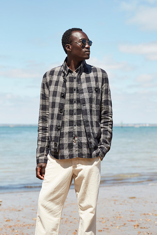 Oliver Spencer Spring 21, look 7. Dark check flannel shirt and cream trousers at the shoreline.
