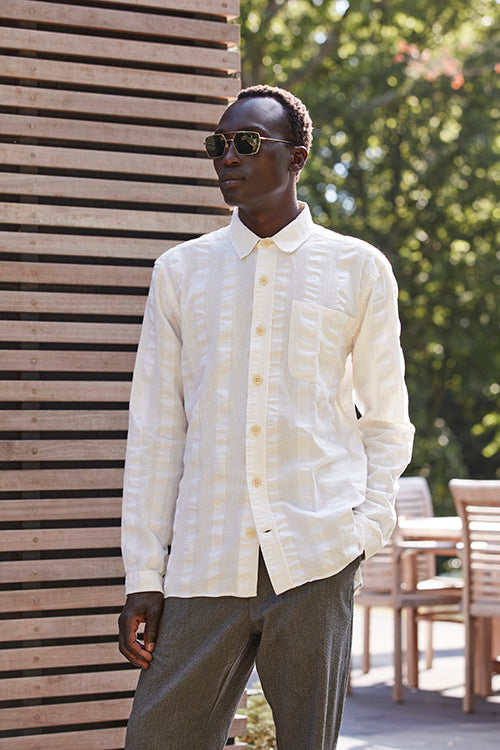 Oliver Spencer Spring 21, look 17. Cream shirt and pale trousers against vertical wood panelling.