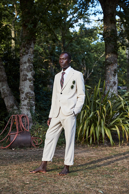 Oliver Spencer Spring 21, look 24. Ivory suit on a path through tropical planting.